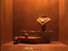 a display case with a necklace and ring on it's stand in front of a brown wall