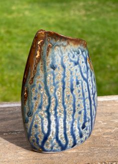 a blue and brown vase sitting on top of a wooden table next to a green field