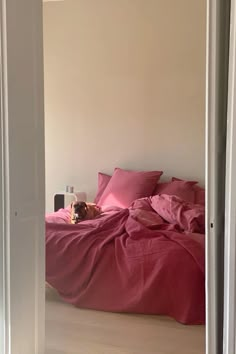 a bed with pink sheets and pillows in a white room next to an open door