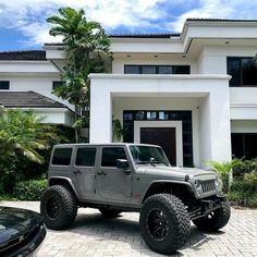 a gray jeep parked in front of a white house with palm trees on the driveway