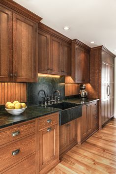 a large kitchen with wooden cabinets and black counter tops, along with a bowl of fruit