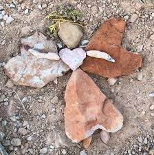 four rocks arranged in the shape of hearts on top of dirt and gravel with plants growing out of them