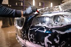 a car being painted with white paint and spray on it's headlight, while someone is waxing the hood