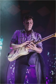 a man playing an electric guitar on stage at a music festival with purple lighting behind him