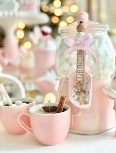 a pink cup filled with hot chocolate and marshmallows next to a candy jar