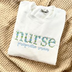 a white t - shirt with blue flowers and the word nurse on it is laying on a piece of fabric