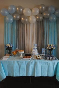 a table topped with cake and balloons next to a wall covered in blue drapes