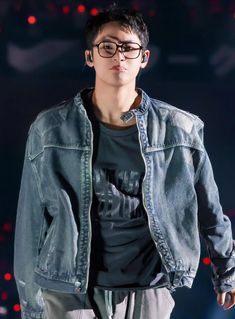 a young man wearing glasses and a denim jacket is walking down the runway at night