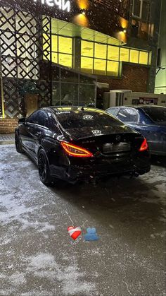 a black car parked in front of a building with snow on the ground next to it