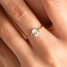 a woman's hand wearing a gold ring with a white diamond in the center