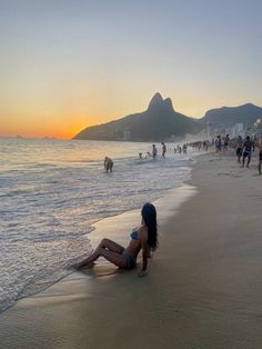 a woman laying on top of a sandy beach next to the ocean with people in the background