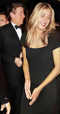 a woman in a black dress standing next to a man in a tuxedo