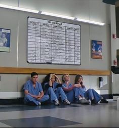 four people in scrubs sitting on the floor next to a wall with a sign