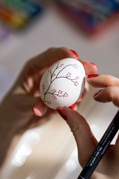 a woman is painting an egg with red flowers on it and holding a black marker