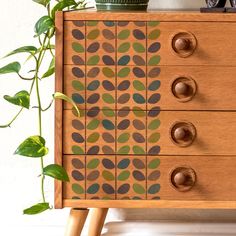 a wooden dresser with leaves painted on the front and sides, sitting next to a potted plant