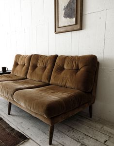 a brown couch sitting on top of a wooden floor next to a white painted wall