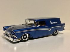 an old model blue car with chrome rims sitting on a white table next to a wall