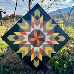 a patchwork quilt sitting on top of a grass covered field next to a tree