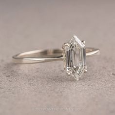 a yellow gold ring with an emerald cut diamond in the center, on a gray surface