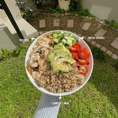 a white bowl filled with rice, meat and veggies on top of green grass