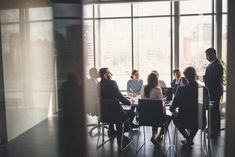 a group of people sitting around a table in front of large windows with the sun shining through them