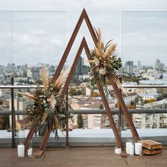 two tall wooden stands with flowers and greenery on them in front of a cityscape