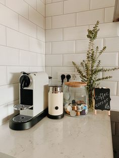 a coffee maker sitting on top of a counter next to a potted plant and chalkboard