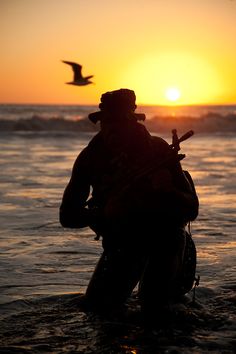 a man standing in the water with a bird flying over his head and holding a fishing rod