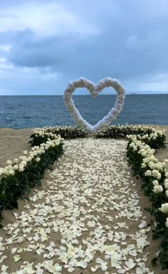 a heart - shaped flower arrangement on the beach with petals in the foreground and water in the background