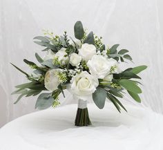 a bouquet of white roses and greenery sits on a round tableclothed surface