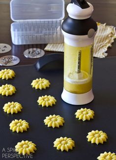 some yellow cookies are on a table next to a bottle and plastic container with the lid open