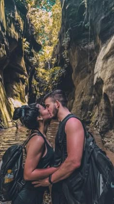 a man and woman kissing while standing in the water near a cliff face each other