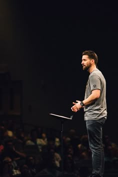 a man standing at a podium in front of an audience with his hands folded out