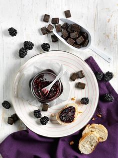 a white plate topped with food next to a bowl filled with jelly and blackberries