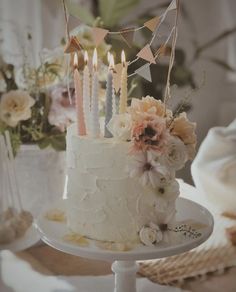 a white cake with flowers and candles on it sitting on a table next to other decorations