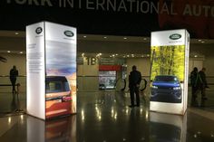 two people standing in front of an exhibit booth with cars on display at the show