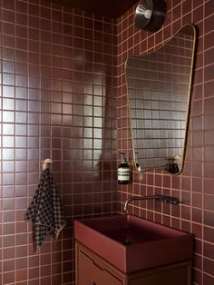 a bathroom with red tiles and a mirror above the sink is shown in this image