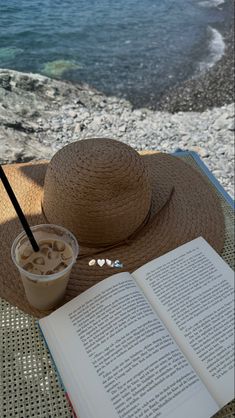 an open book sitting on top of a table next to a straw hat and drink