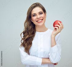 a woman holding an apple in her right hand and smiling at the camera while standing against a white background