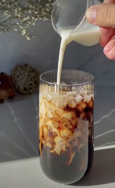 someone pouring milk into a glass filled with food