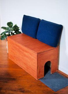 a wooden bench with two blue cushions on it and a potted plant in the corner