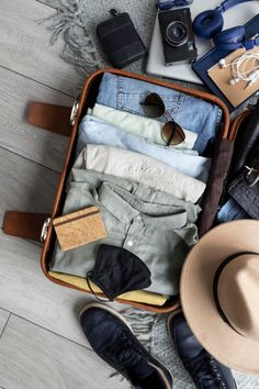 an open suitcase filled with clothes and hats on top of a wooden floor next to other items