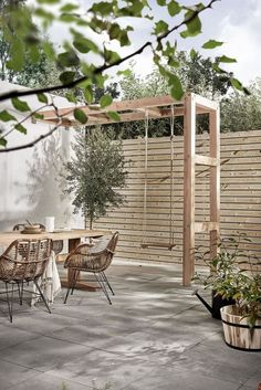 an outdoor dining area with wooden furniture and plants on the table, next to a pergolated wall