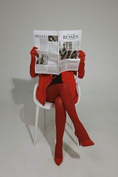 a woman sitting in a white chair while reading a newspaper with red stockings on her legs