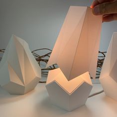 a person is holding an object in front of three paper structures that are shaped to look like geometric shapes