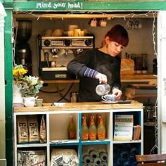 a woman pours tea into a cup in front of a storefront with shelves