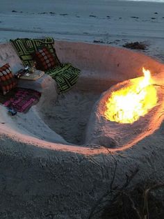 a fire pit made out of sand with pillows and blankets around it on the beach