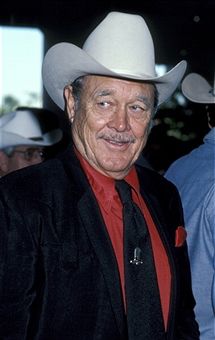 an older man in a suit and tie wearing a cowboy hat with other men behind him