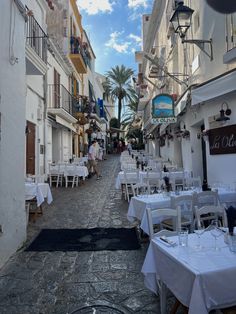 an empty street with tables and chairs in the middle, surrounded by white buildings on both sides