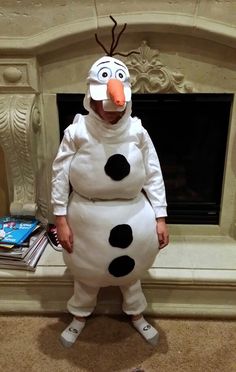 a child dressed as a snowman standing in front of a fire place with books